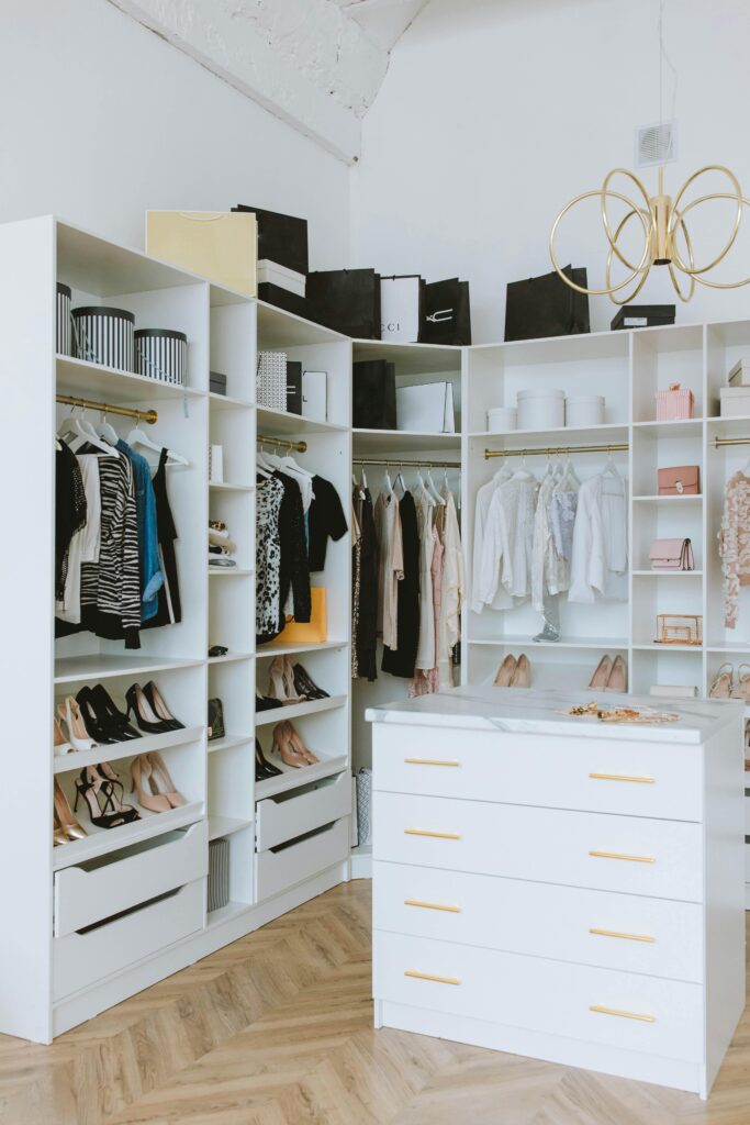 A stylish walk-in closet featuring luxury clothing, shoes, and accessories, with elegant shelving and chandeliers.